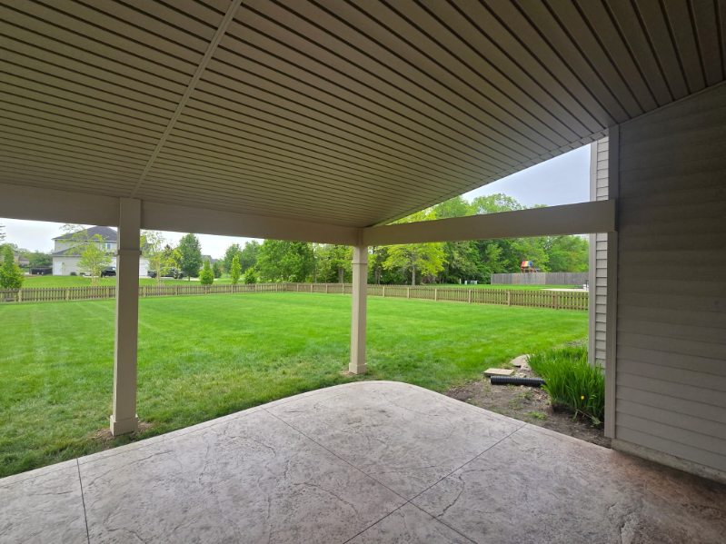 Stamped concrete patio under a covered porch overlooking a fenced backyard in Northern Indiana