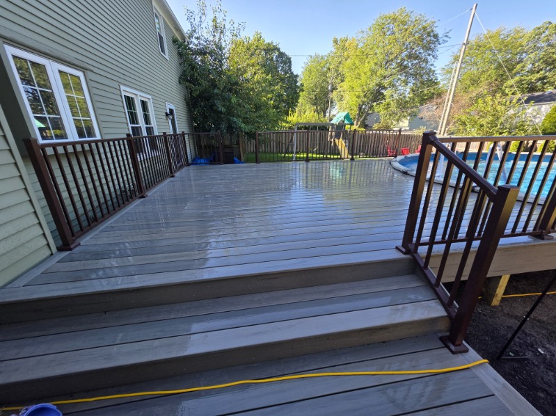 Large gray composite pool deck with bronze aluminum railing and wide steps built beside an above ground pool in Northern Indiana