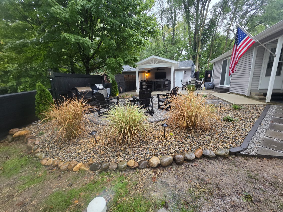 Covered patio addition with concrete floor, outdoor dining area, black privacy fence, and landscaped rock garden