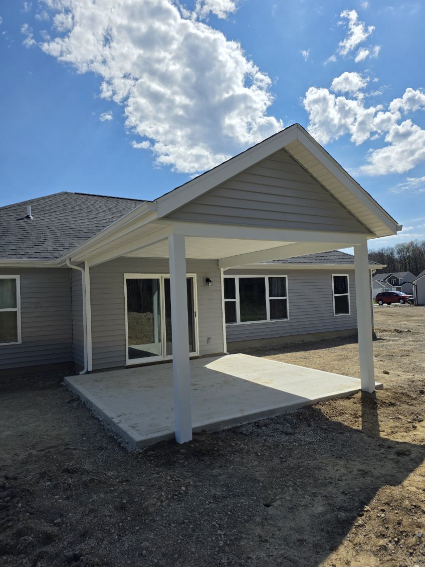 Gable roof covered porch with white columns and new concrete slab on a gray vinyl sided home
