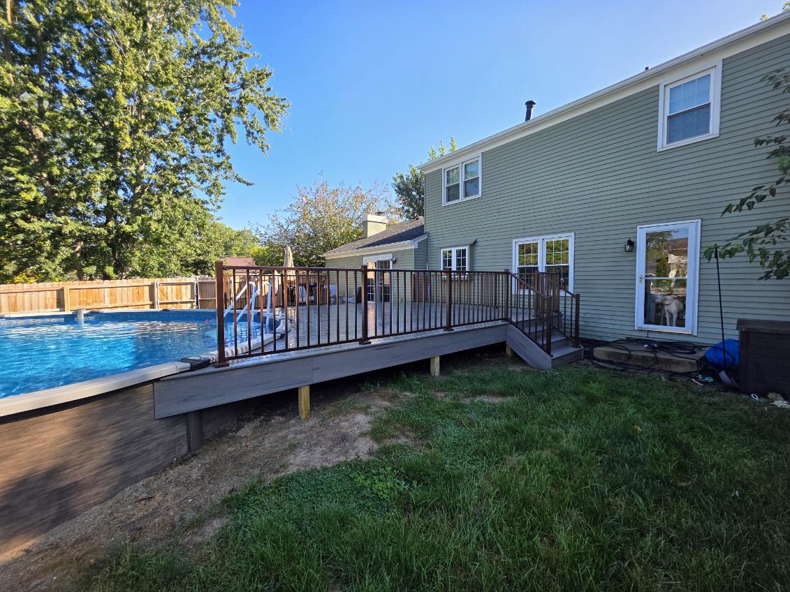 Composite deck with bronze aluminum railing and steps attached to an above ground pool in a fenced backyard