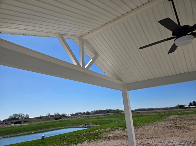 Underside of a covered porch with white beadboard ceiling, exposed truss and ceiling fan overlooking a pond