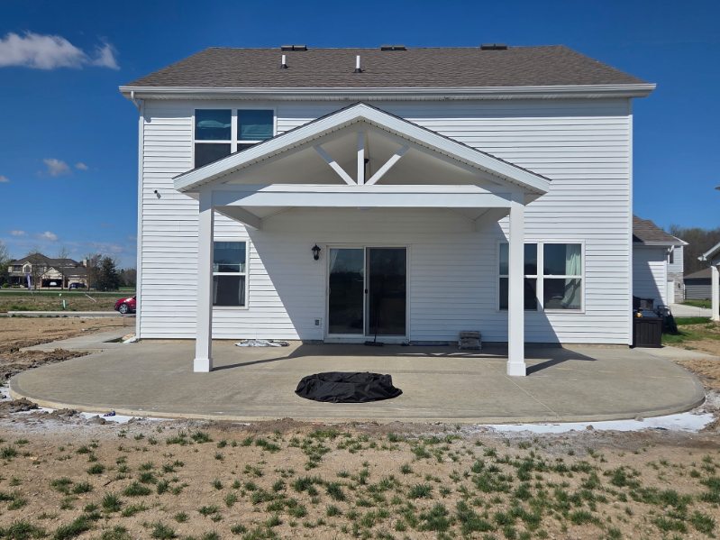 Rear covered porch addition with gable roof, white columns and broom finished concrete patio in Northern Indiana