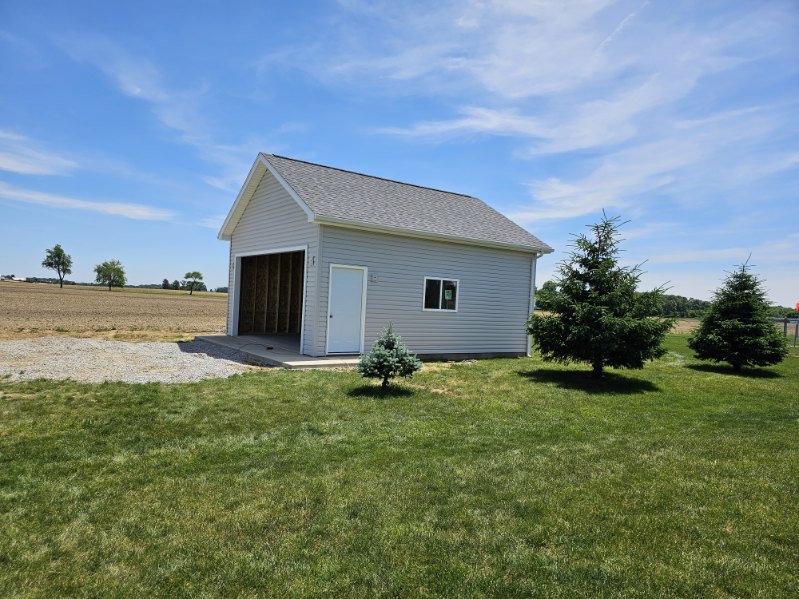 White detached pole barn garage with side entry door and gravel drive