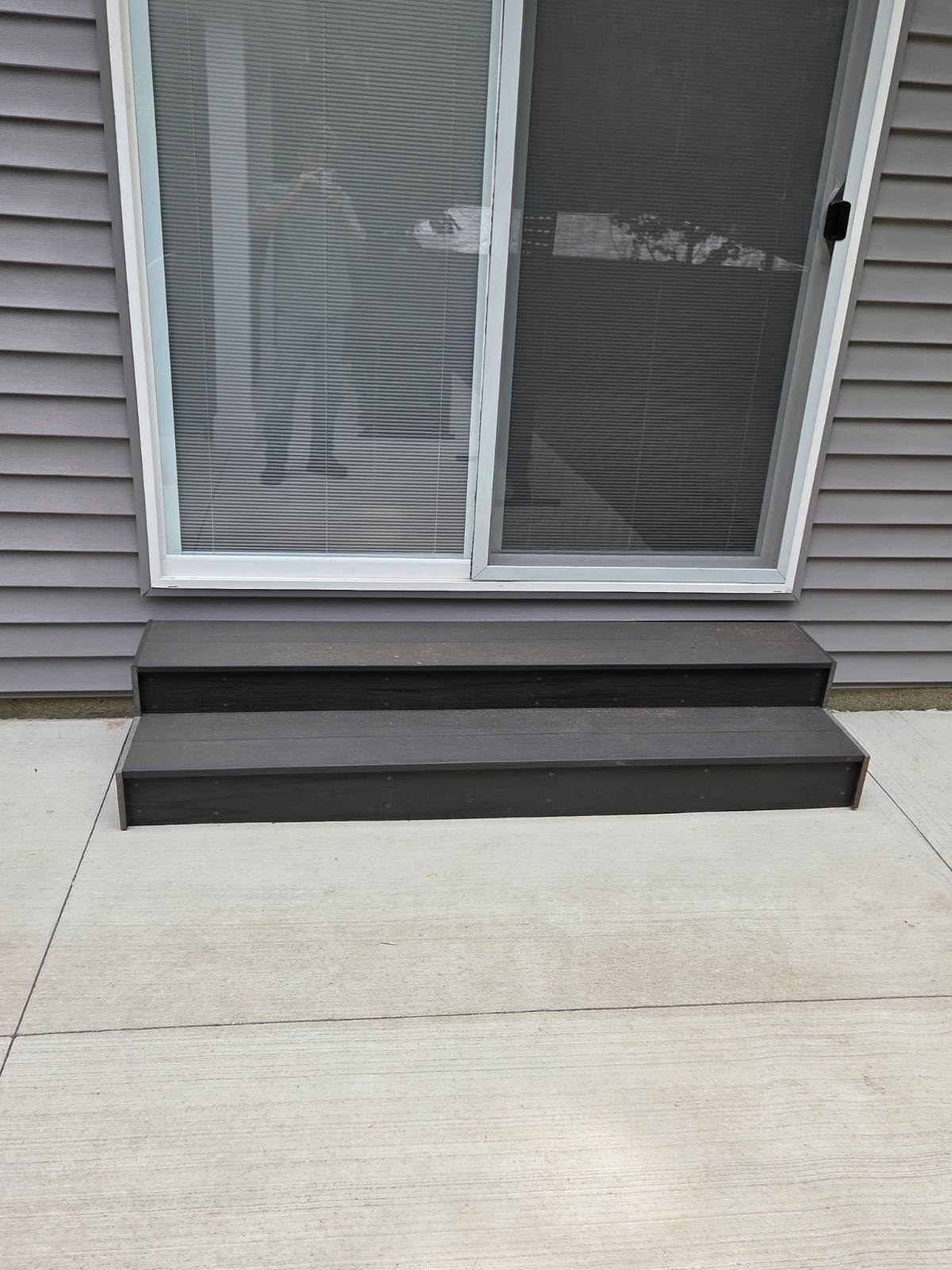 Composite steps with dark decking at a sliding patio door built by T&J Construction