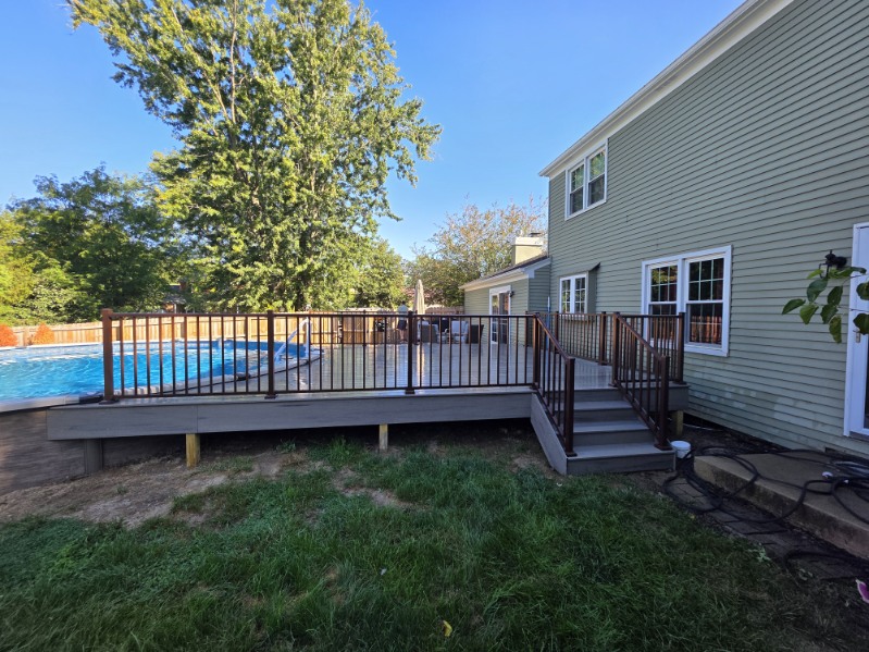 Backyard view of a new composite pool deck with bronze railing and steps attached to a green sided two story home