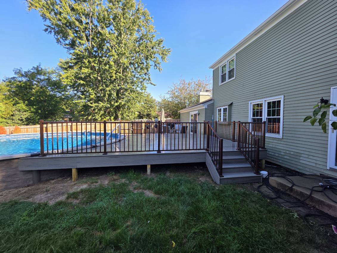 Side view of a composite pool deck with bronze railing, wide stair landing, and pool ladder
