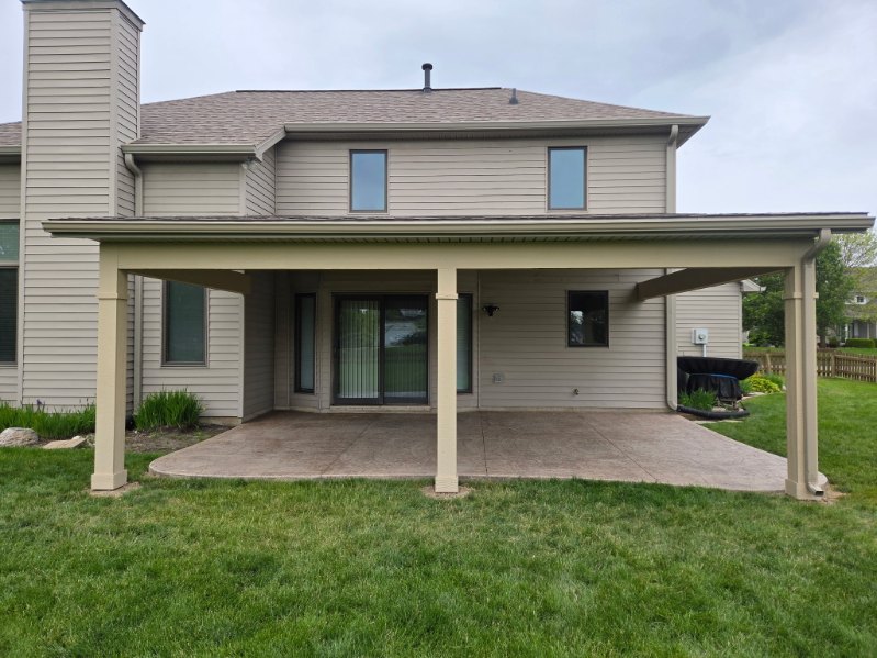 Attached covered patio roof with tan columns over a stamped concrete pad behind a two story home