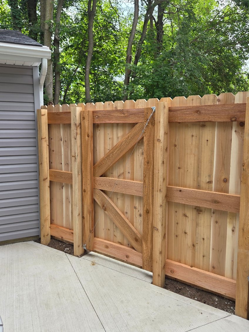 Cedar privacy fence panels and braced gate installed along a concrete driveway