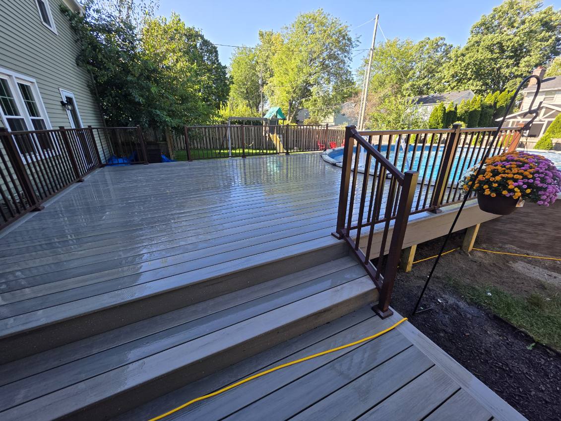 Gray composite pool deck with bronze aluminum railing, wide steps, and fall mums overlooking an above ground pool