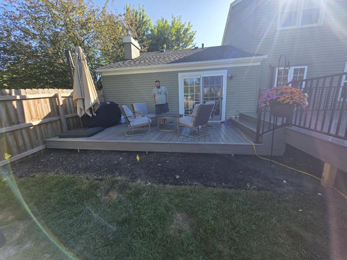 Low profile composite patio deck with grill and seating area behind a green sided home in Northern Indiana