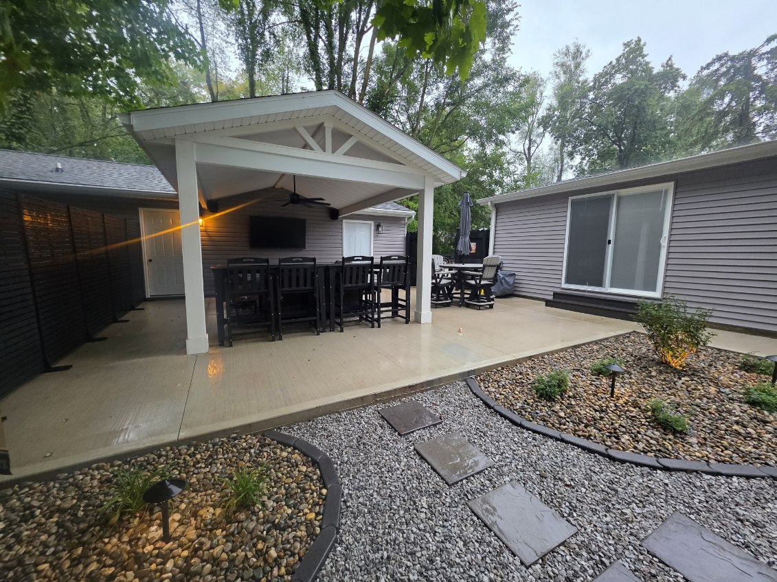 Backyard entertainment space with covered patio, fire pit seating, American flag, landscaping, and concrete hardscaping