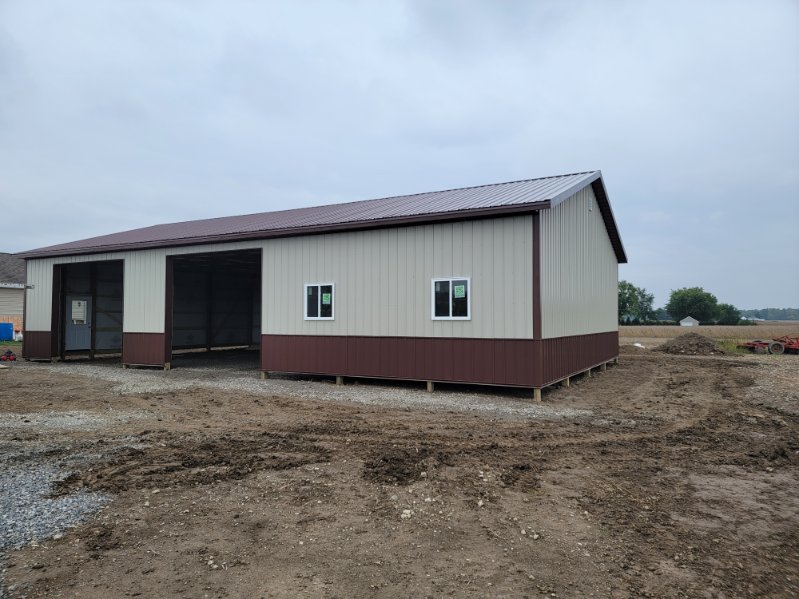 Two tone pole barn with tan siding, brown wainscot, and open drive through bay