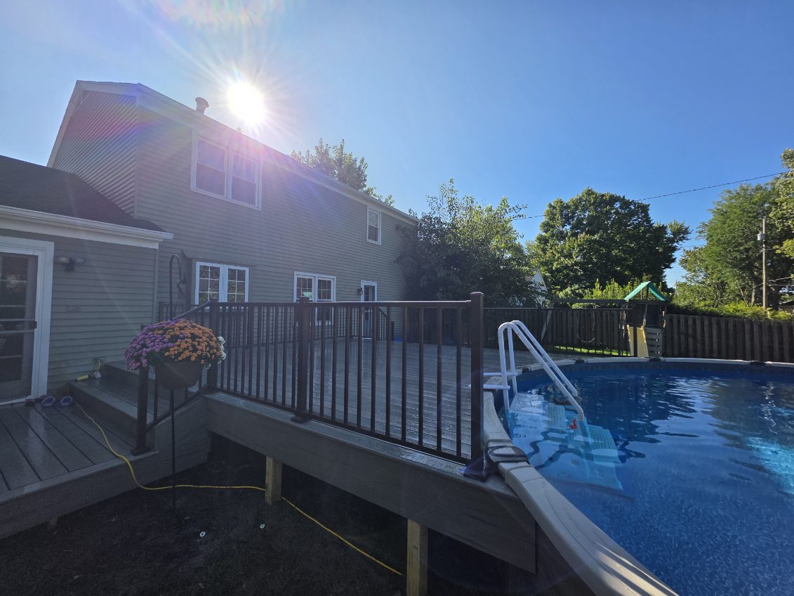 Poolside composite deck wrapping an above ground pool with bronze aluminum railing and pool ladder