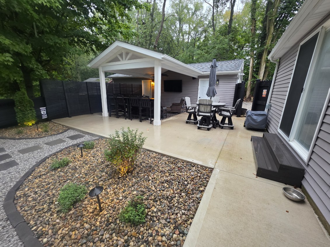 Covered backyard patio pavilion with white posts, outdoor kitchen bar, TV, ceiling fan, and concrete pad in Northern Indiana