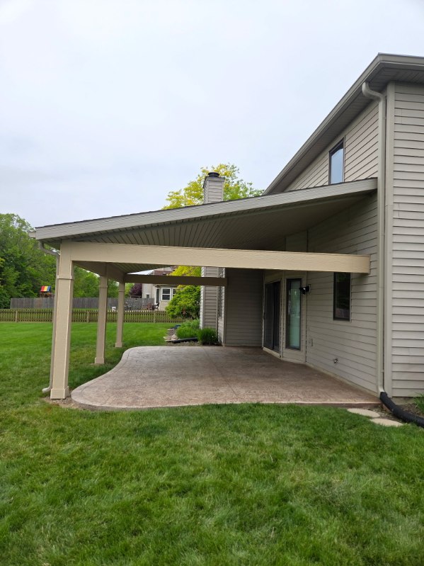 Side view of a covered patio structure with tan posts and stamped concrete built by T&J Construction