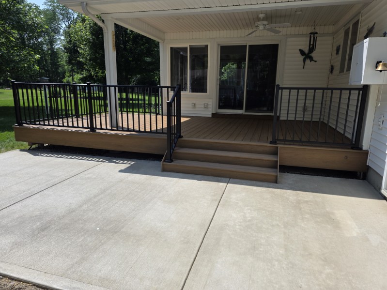 Covered composite deck with ceiling fan, black railing, and steps down to a concrete patio