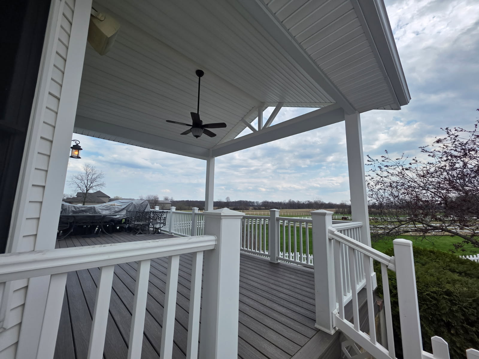 Covered composite deck with gray decking, white railing, and ceiling fan overlooking pasture