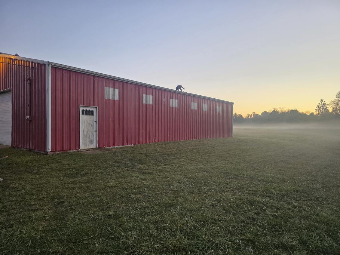 Red metal pole barn at sunrise with crew installing new metal roofing