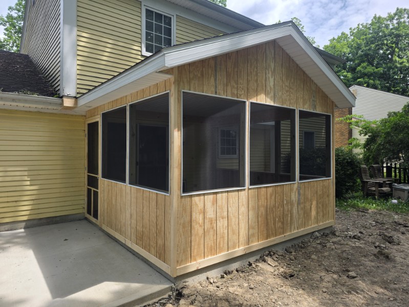 Screened porch addition with cedar siding, new gable roof, and fresh concrete patio