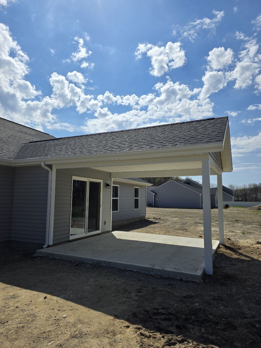 Shed style covered porch with white columns and concrete pad addition on a gray sided home